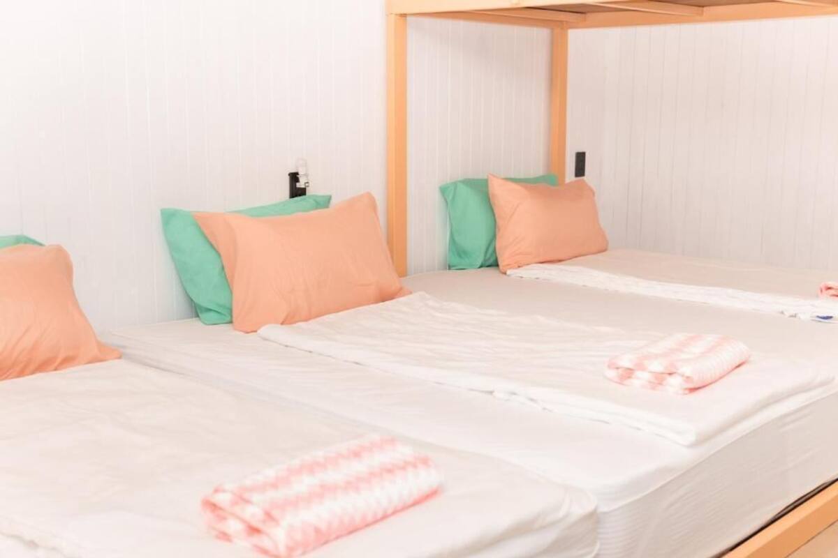Habitación de hotel con dos camas, cada una con cabecero de madera, ropa de cama blanca y almohadas verdes y melocotón.