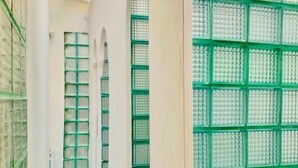Un pasillo con paredes blancas, rejas de ventana verdes y una estructura tipo cuadrícula a la derecha.