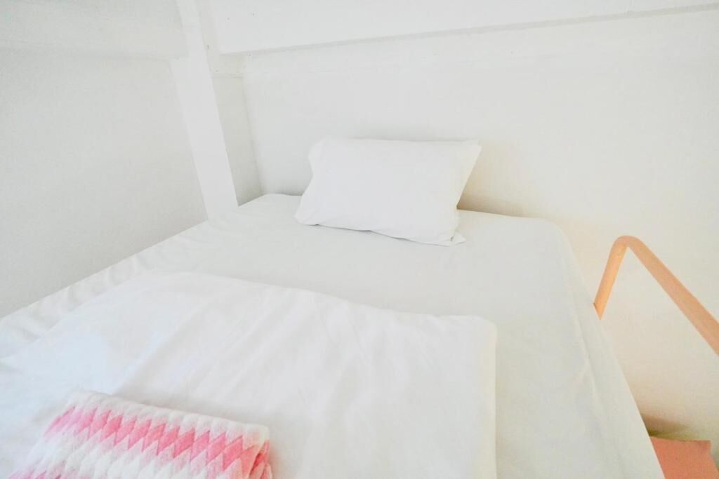 Un lit simple avec un oreiller blanc et une couverture à motifs roses et blancs.
