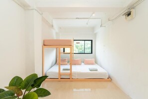 Une petite pièce lumineuse, avec un lit superposé, une fenêtre et une plante.