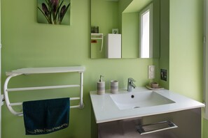 A bathroom with a white sink, a towel rack with a blue towel, a mirror, and a green wall. - Guesthouse "Demeure Olea" (Chérac)