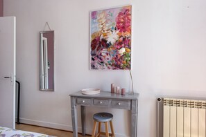 A room with a grey desk, a mirror, a radiator, and a floral painting on the wall. - Guesthouse "Demeure Olea" (Chérac)