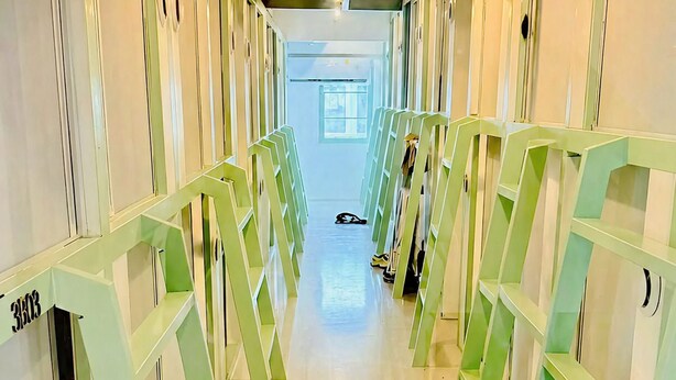 A corridor with green shelving units, a visible door labeled '300', and a shoe on the floor. - Monday Capsule & Thai Traditional Bath  (Bangkok)