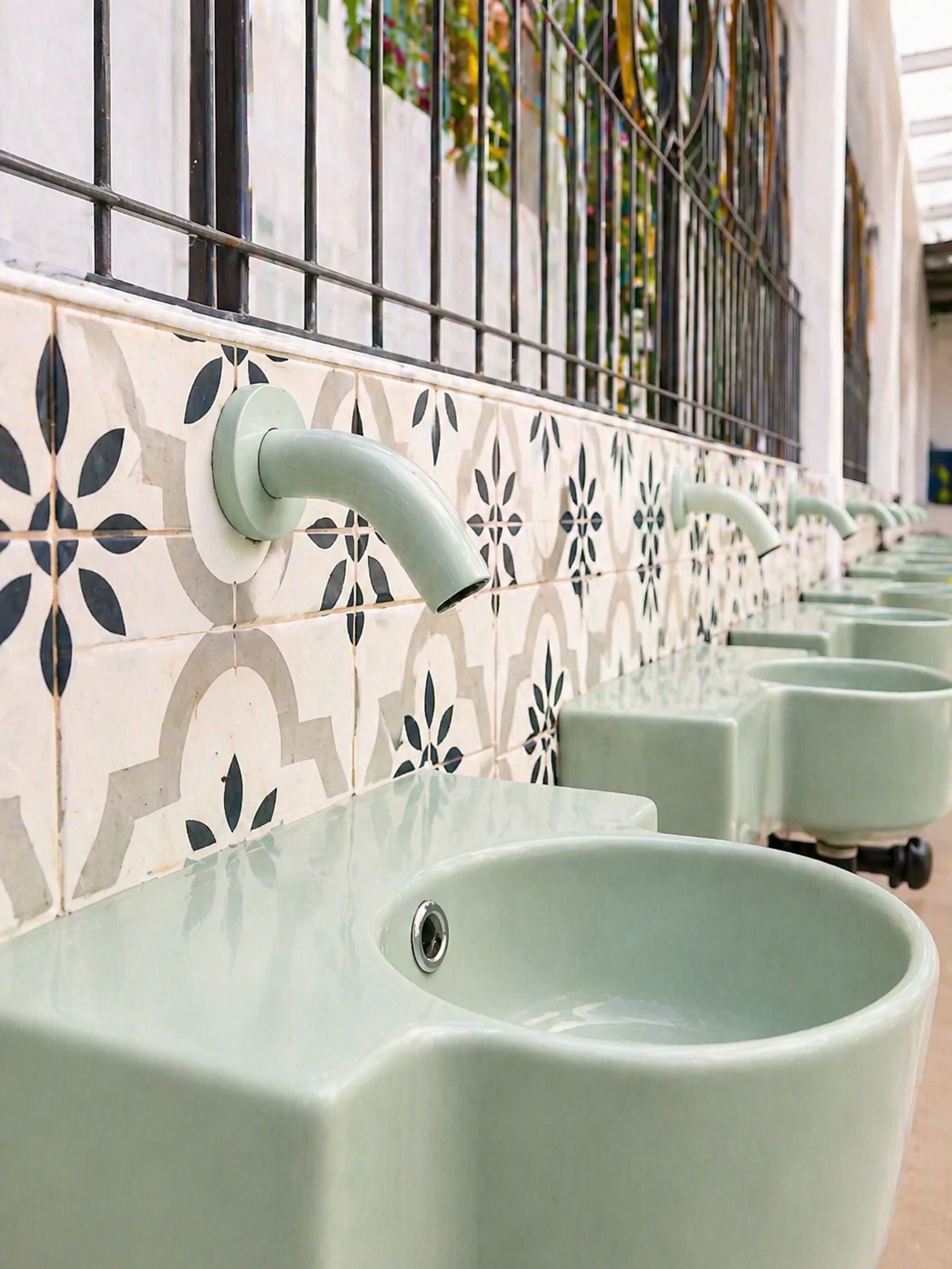 A row of green sinks with a decorative tile wall behind them.