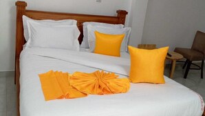 A bed with white bedding, two orange pillows, and a folded orange towel. - Ehtans Hotel And Accommodations (Eldoret)