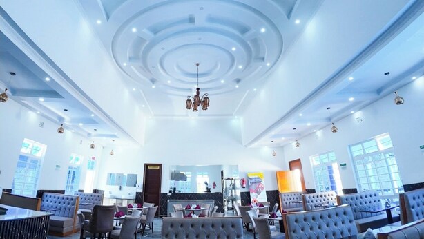 A spacious hotel lobby with a modern ceiling design, seating areas, and a reception desk. - Ehtans Hotel And Accommodations (Eldoret)