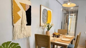 Un coin repas avec une table dressée pour quatre personnes, des chaises en bois avec des coussins bleus, un vase rempli de fleurs et un panier de fruits.