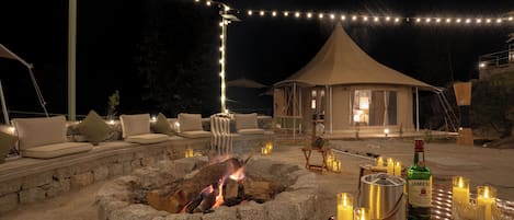 A stone fire pit with a fire, surrounded by outdoor seating and string lights.