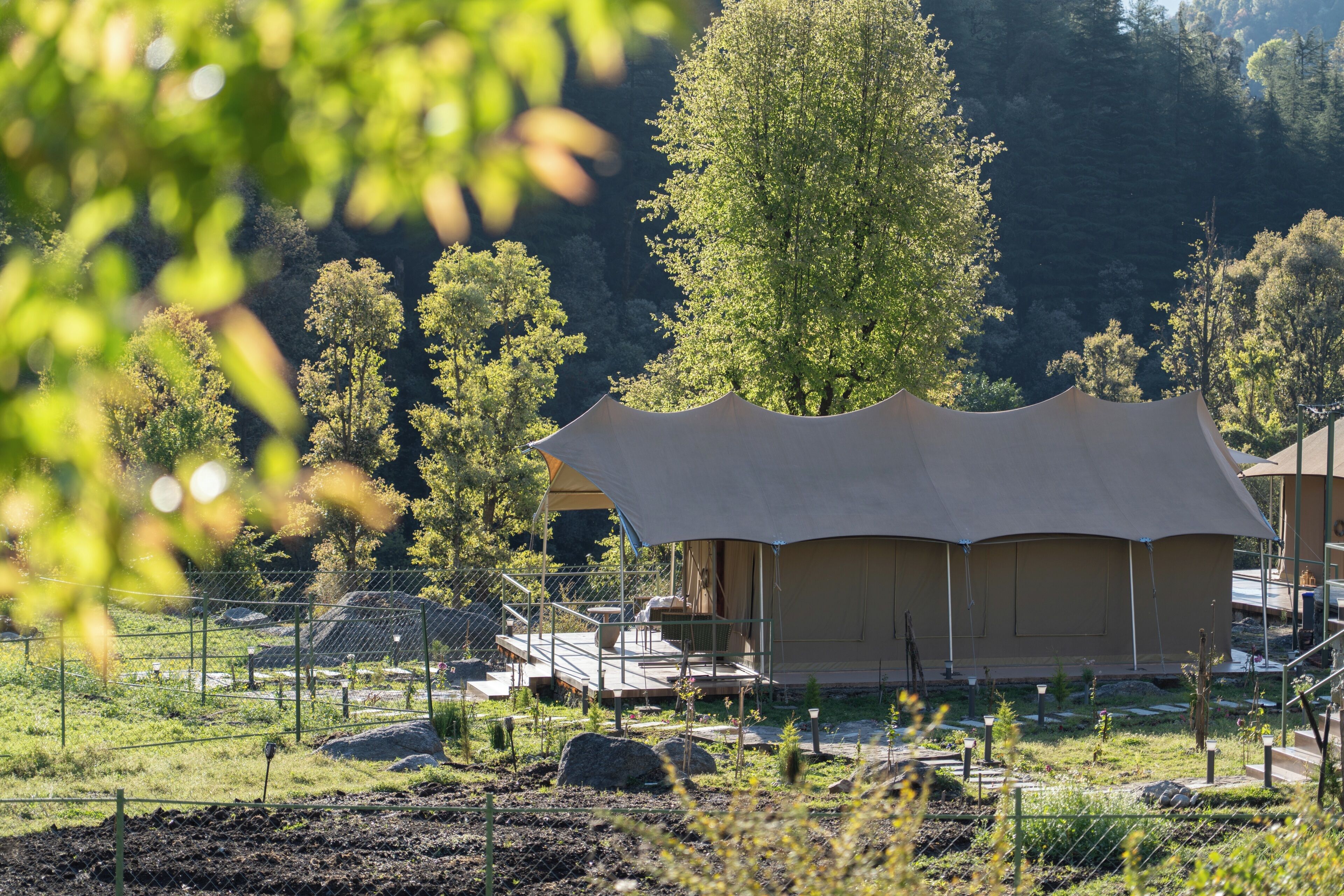A tented accommodation with a deck and outdoor seating, surrounded by trees and a fenced area.
