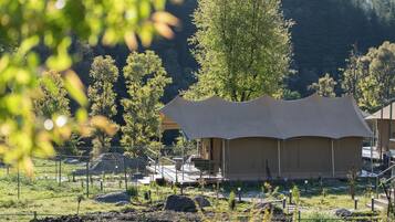 A tented accommodation with a deck and outdoor seating, surrounded by trees and a fenced area.