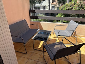 Ein Balkon mit Tisch und vier Stühlen, ein Fliesenboden und Blick auf Gebäude und Grünflächen.