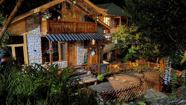 A rustic wooden cabin with a stone facade, a balcony, and a small porch area. - Cozy, Aesthetic Nature Retreat: Feel Your Soul in the Village Soil (Soil)
