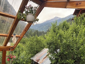 Un invernadero con estructura de madera, una maceta colgante y vistas a un paisaje montañoso.