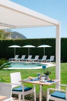 Zona junto a la piscina con sillones reclinables, sombrillas y una mesa lista para comer.