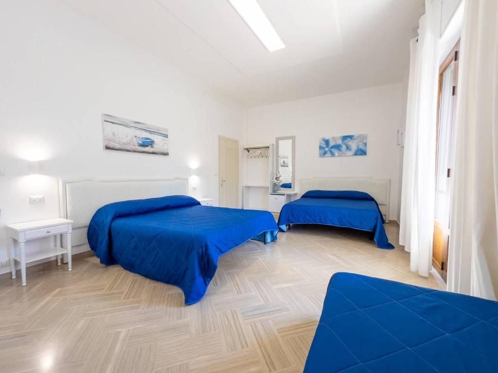 Una habitación de hotel con dos camas, un escritorio blanco, un espejo y obras de arte en las paredes.