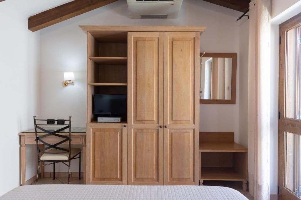 Een slaapkamer met een bed, een bureau met stoel, een kledingkast en een spiegel.