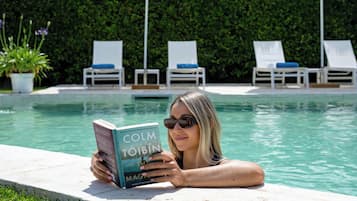 Una persona leyendo un libro de Colm Tóibín junto a una piscina con sillones de descanso y una siega al fondo.