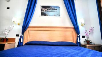 Una habitación de hotel con una cama grande, cortinas azules, un cuadro en la pared y dos mesitas de noche con lámparas.