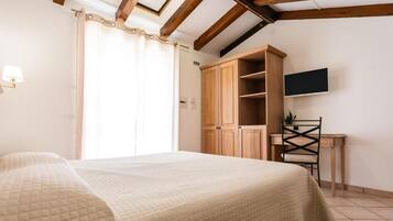 A bedroom with a bed, a desk, a chair, a wardrobe, and a television on the wall.