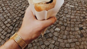 Käsi pitää jälkiruokaa, jossa on suklaakuorrute ja puinen tikku, ja se on asetettu mukulakivipinnalle.