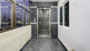 A hallway with a modern elevator, large windows, and a tiled floor. - Deluxe Mini Bypass Nellore Road (Nellore)