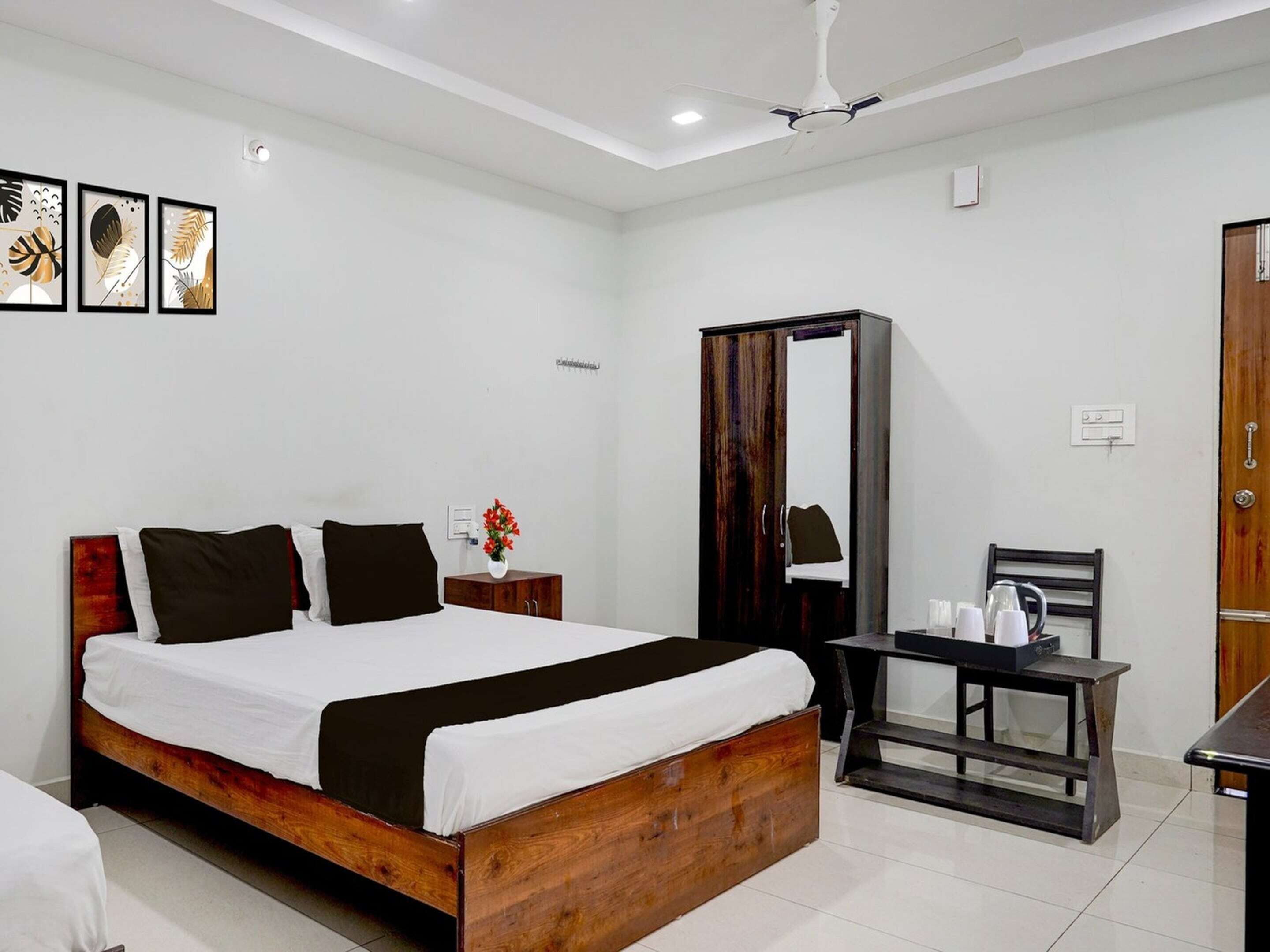 A hotel room with a wooden bed, a desk with a chair, a wardrobe, and framed artwork on the wall.