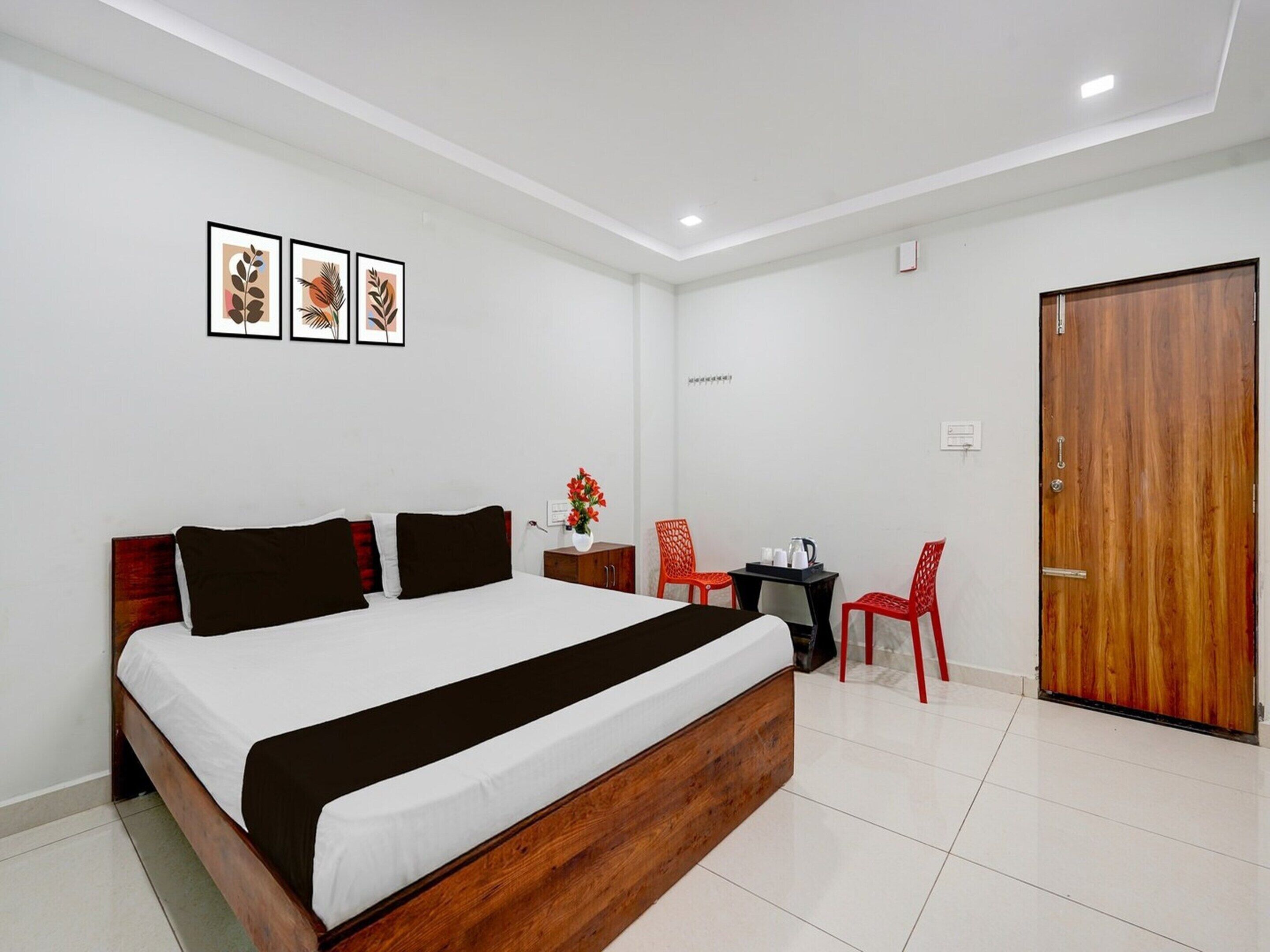 A hotel room with a large bed, a small desk with a chair, a wooden door, and three framed pictures on the wall.