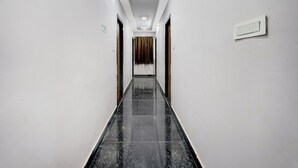 A hallway with white walls, a black marble floor, and a door at the end. - Deluxe Mini Bypass Nellore Road (Nellore)