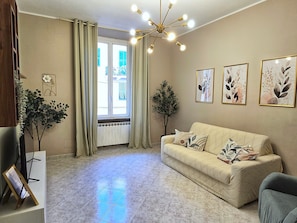 A living room with a sofa, a small table, a plant, and a window with curtains.