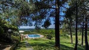 Une piscine entourée d’arbres, un sentier en pierre et une vue sur le paysage.