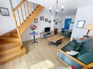 Ein Wohnzimmer mit Holztreppe, Essbereich, Sofa und einer Chandelieber.