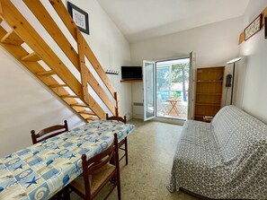 A room with a wooden staircase, a dining table with chairs, a bed, and a sliding glass door leading to an outdoor area. - Quiet apartment near beach - 4 guests (Bretignolles-sur-Mer)
