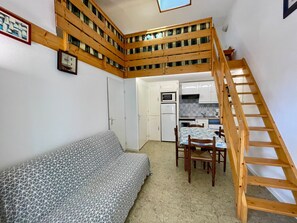 A compact living space with a wooden staircase, a sofa, a dining table, and a kitchenette. - Quiet apartment near beach - 4 guests (Bretignolles-sur-Mer)