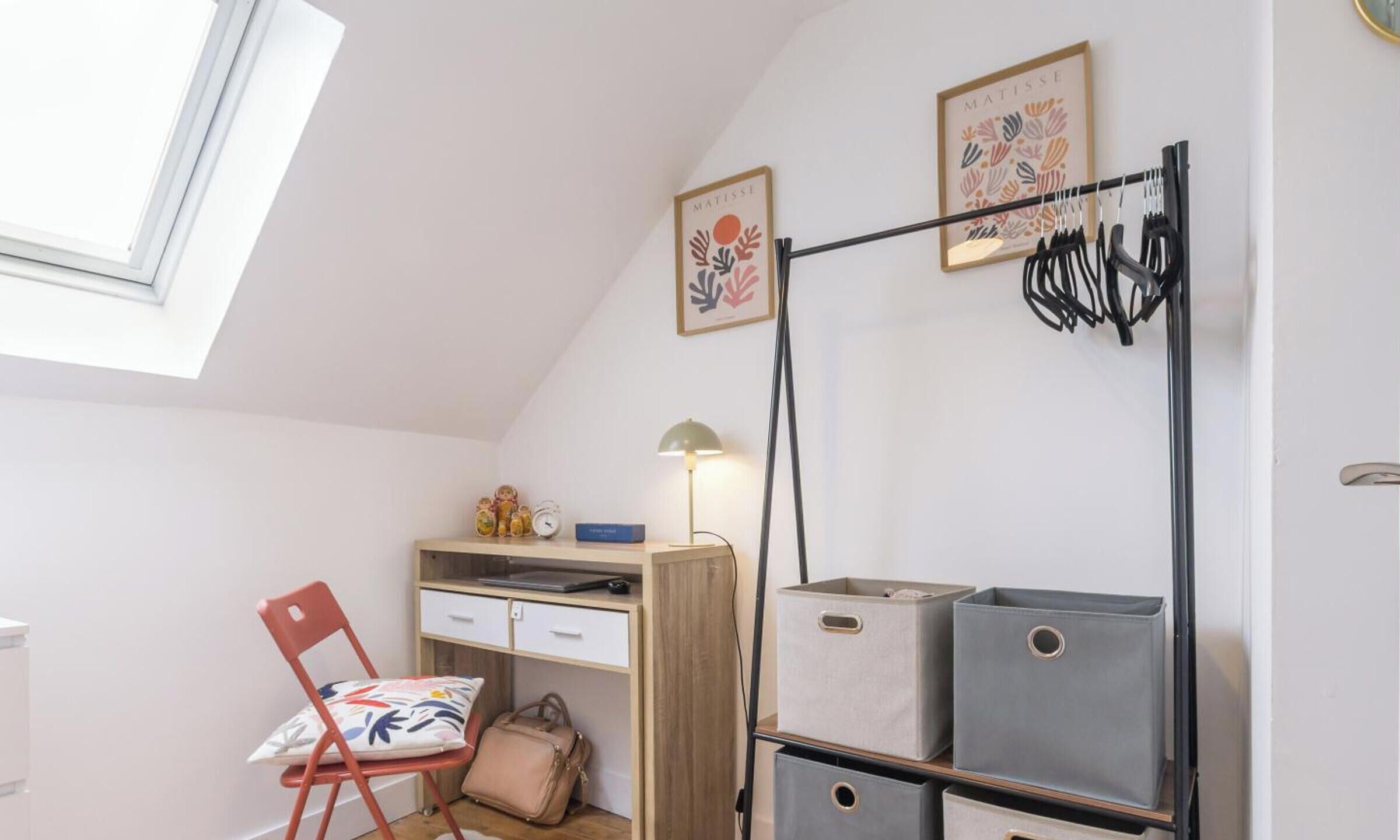 A room with a desk, chair, lamp, wall art, and storage boxes.
