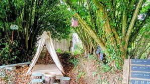 Un espacio de descanso al aire libre de estilo rústico con taburetes de madera, un banco de madera y una pizarra con texto.