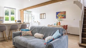 Una sala de estar con un sofá, un comedor con sillas, una escalera y un cuadro en la pared.