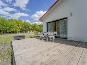 A wooden deck with outdoor furniture, a modern building with a glass door, and a view of trees and a fence in the background. - Comfortable house near beaches - 3 bdrms. (Mimizan)