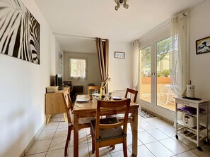 Un comedor con una mesa preparada para dos personas, un televisor y una ventana con cortinas.