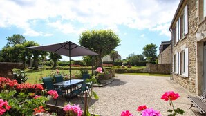 A patio with a table and chairs, surrounded by a garden with pink flowers. - Beautiful stone house, private garden in the heart of Cotentin (Bricquebec-en-Cotentin)