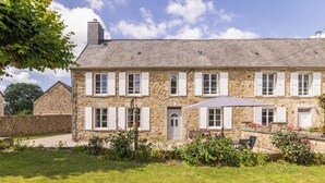 A stone house with a grey roof, multiple windows with shutters, a door, and a small garden with flowers and a bench. - Beautiful stone house, private garden in the heart of Cotentin (Bricquebec-en-Cotentin)