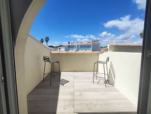 Ein Balkon mit zwei Metallstühlen, einem Fliesenboden und Blick auf Gebäude im Hintergrund.