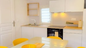A compact kitchen with a white countertop, a sink, a stove, and a dishwasher. There are yellow chairs around a white table. - Mobile home, AC - 5 guests (Sainte-Marie)