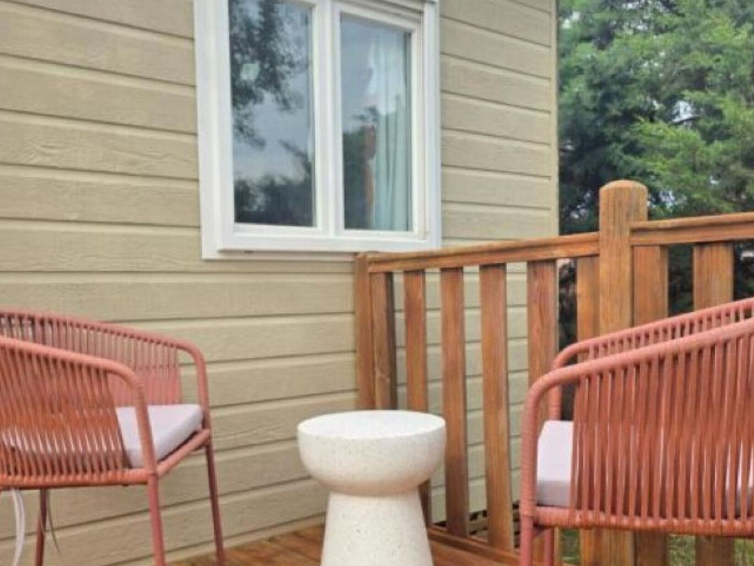 A wooden deck with two wicker chairs and a small white stool.