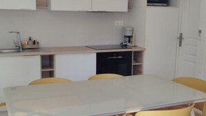 Een kleine keuken met een spoelbak, magnetron en koffiezetapparaat. Er is een eettafel met stoelen.