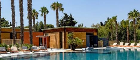 Un espace piscine avec des chaises longues, un petit bâtiment et de grands palmiers.