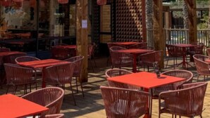 Een buitenterras met rode tafels en rieten stoelen, een pergola van hout en uitzicht op de straat.