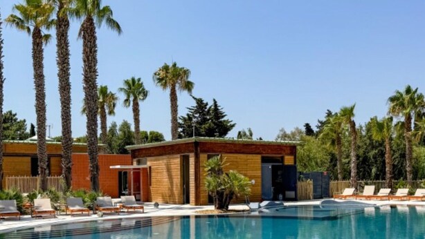 A pool area with lounge chairs, a small building, and tall palm trees. - Mobile Home with Terrace and AC - 6 guests (Sainte-Marie)