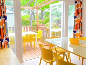 A covered outdoor area with a table and chairs, a view of greenery, and a wooden deck. - Mobile Home with Terrace and AC - 6 guests (Sainte-Marie)