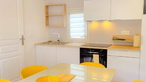 A compact kitchen with white cabinets, a sink, a stove, and a dining table with yellow chairs. - Mobile Home with Terrace and AC - 6 guests (Sainte-Marie)