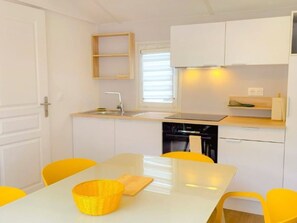 A compact kitchen with white cabinets, a sink, a stove, and a dining table with yellow chairs. - Mobile Home with Terrace and AC - 6 guests (Sainte-Marie)